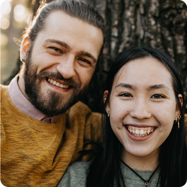 一对微笑的情侣倚靠在树干上。